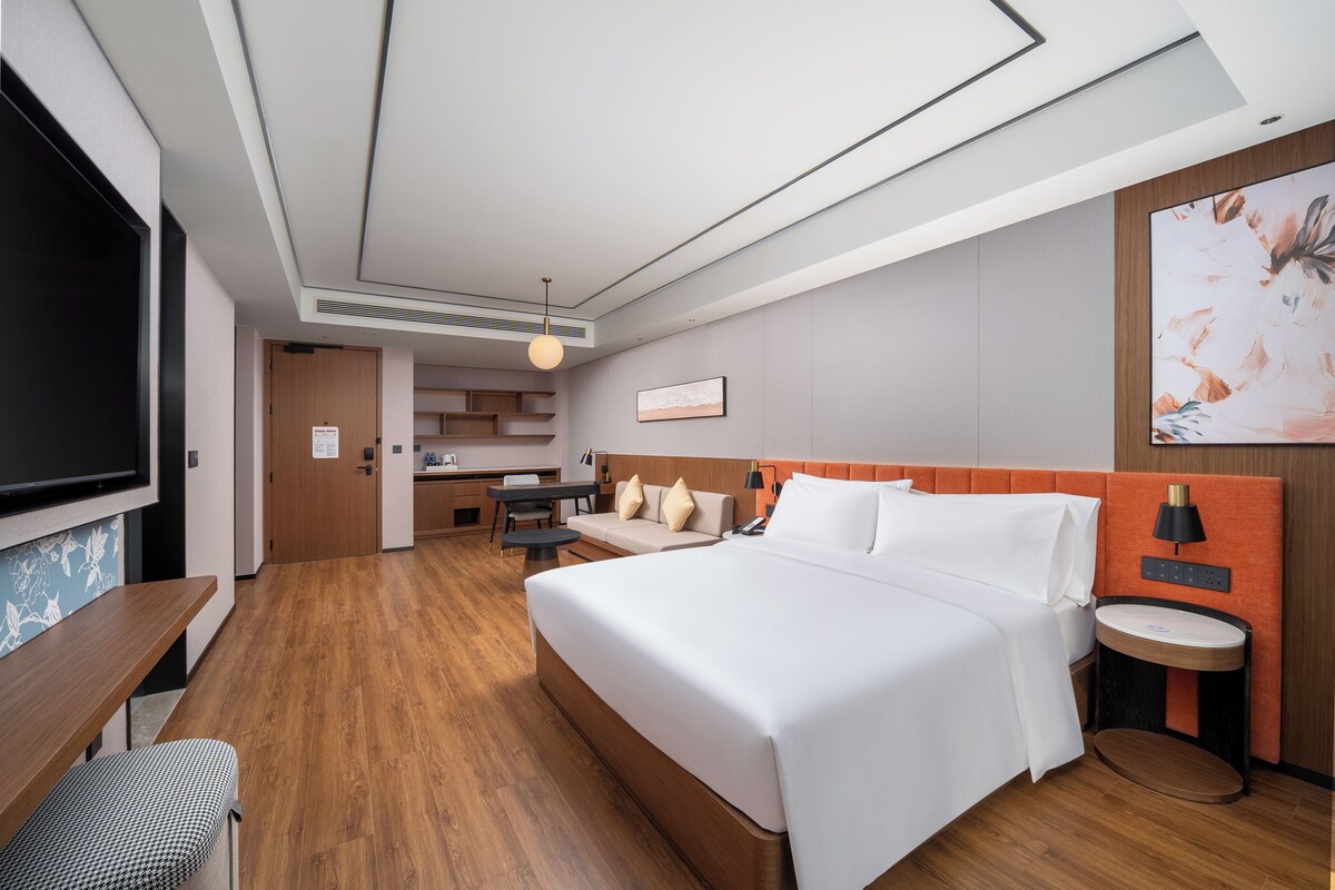A hotel room with a large bed, a desk, a chair, a TV, and a painting on the wall.