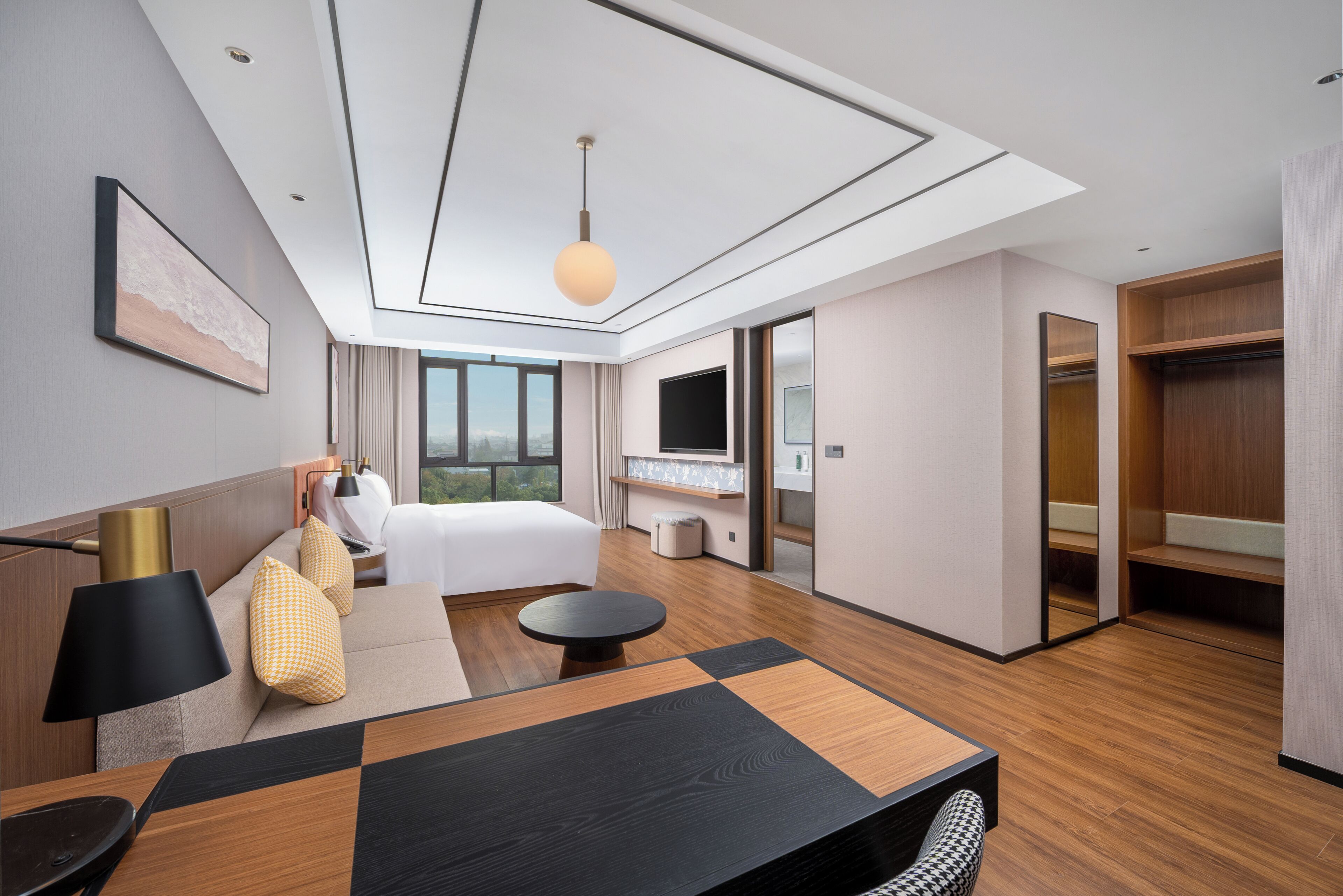 Une chambre d’hôtel moderne équipée d’un grand lit, d’un bureau, d’une table ronde, d’un canapé, d’une télévision et d’une armoire.