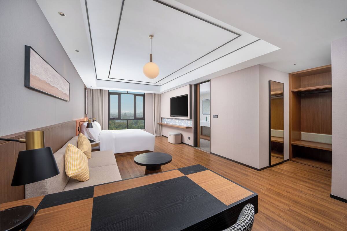 Une chambre d’hôtel moderne équipée d’un grand lit, d’un bureau, d’une table ronde, d’un canapé, d’une télévision et d’une armoire.