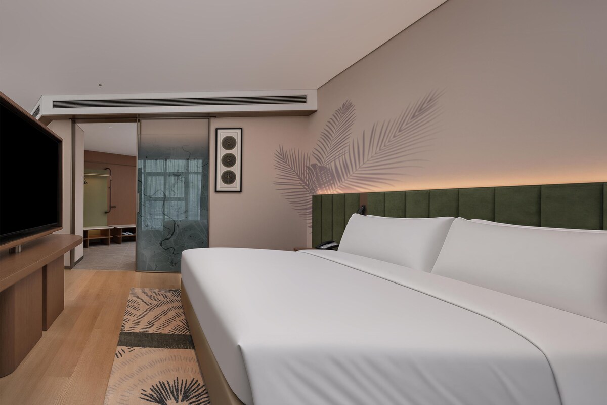 Habitación de hotel moderna con una cama grande, televisión y cabecero verde.