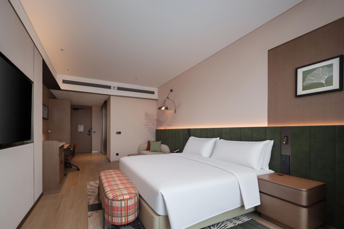 A modern hotel room with a large bed, bedside tables, a desk, and a television.