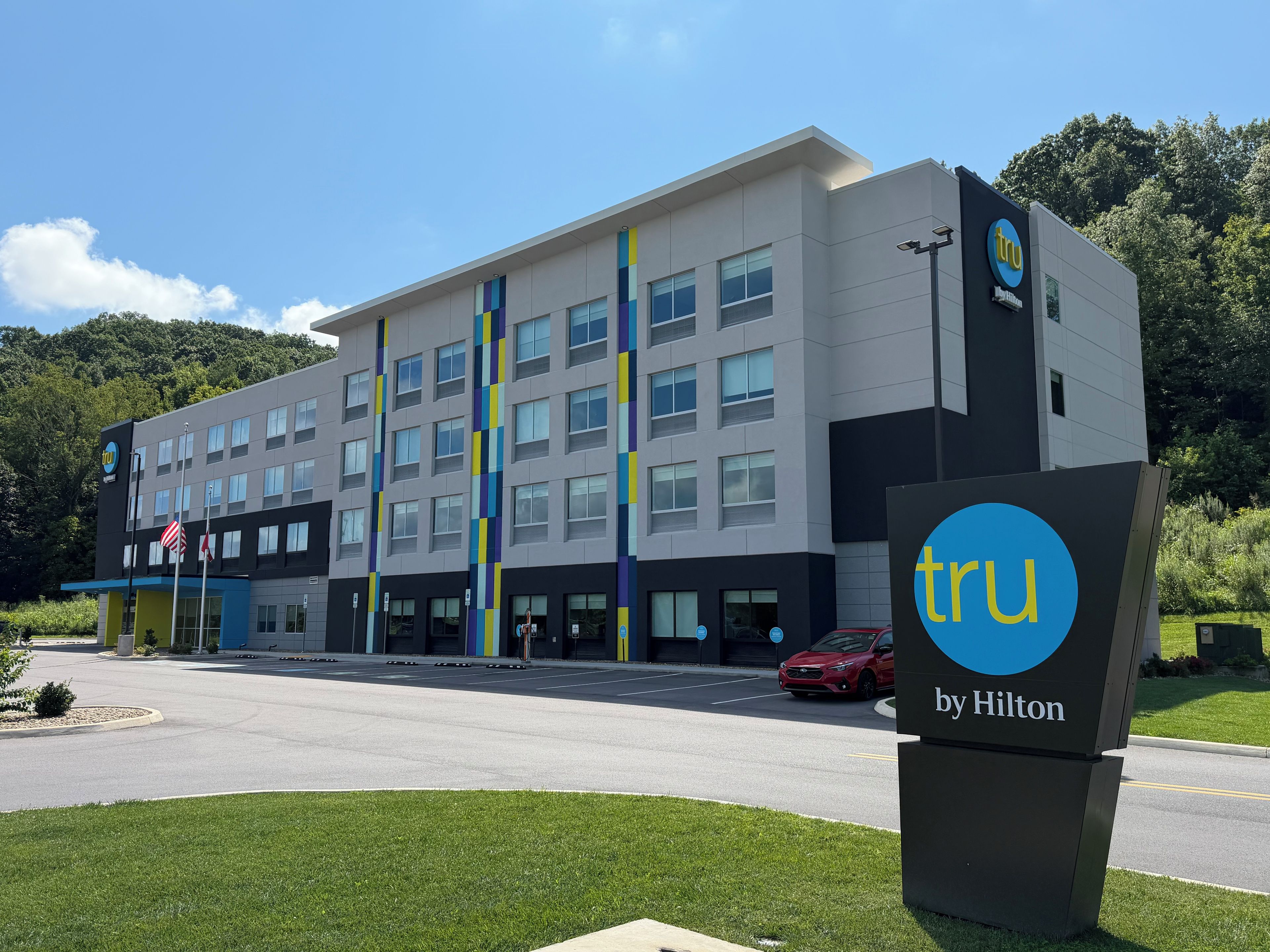Un bâtiment moderne abritant un hôtel, avec une enseigne indiquant « tru by Hilton » et un parking situé devant.