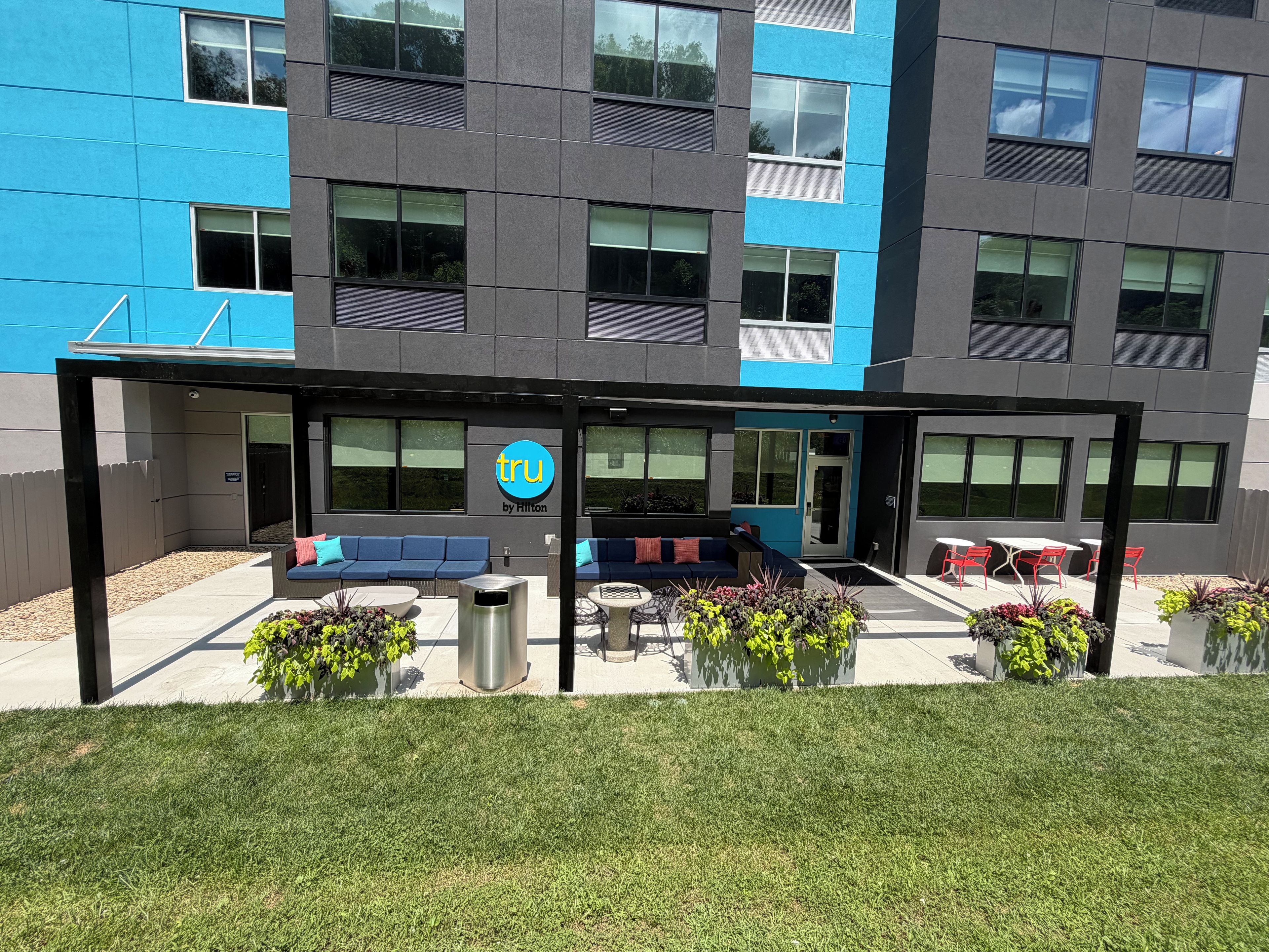 A hotel exterior with a blue and gray facade, outdoor seating area with blue sofas, and potted plants.