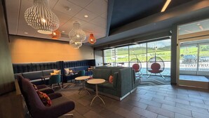 Un espace de détente moderne, doté de différents types de sièges, offrant une vue dégagée grâce à de grandes fenêtres et agrémenté d’un éclairage décoratif.