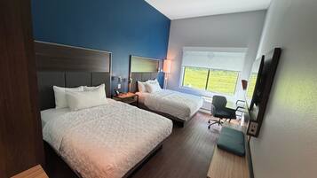 Een hotelkamer met twee bedden, een bureau, een stoel, een televisie en een raam met uitzicht op groen.