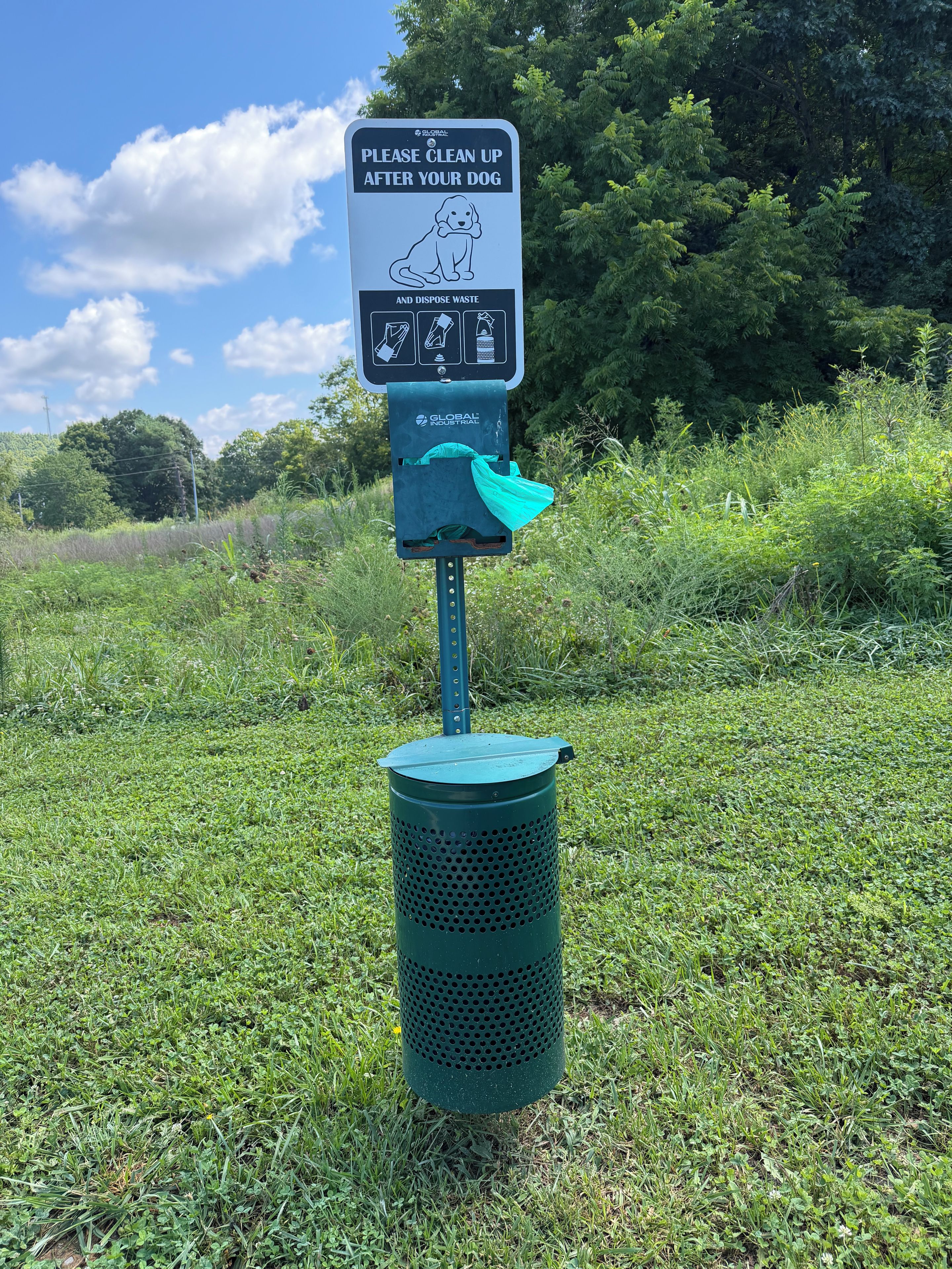 A public trash bin with a sign instructing to clean up after dogs and dispose of waste.