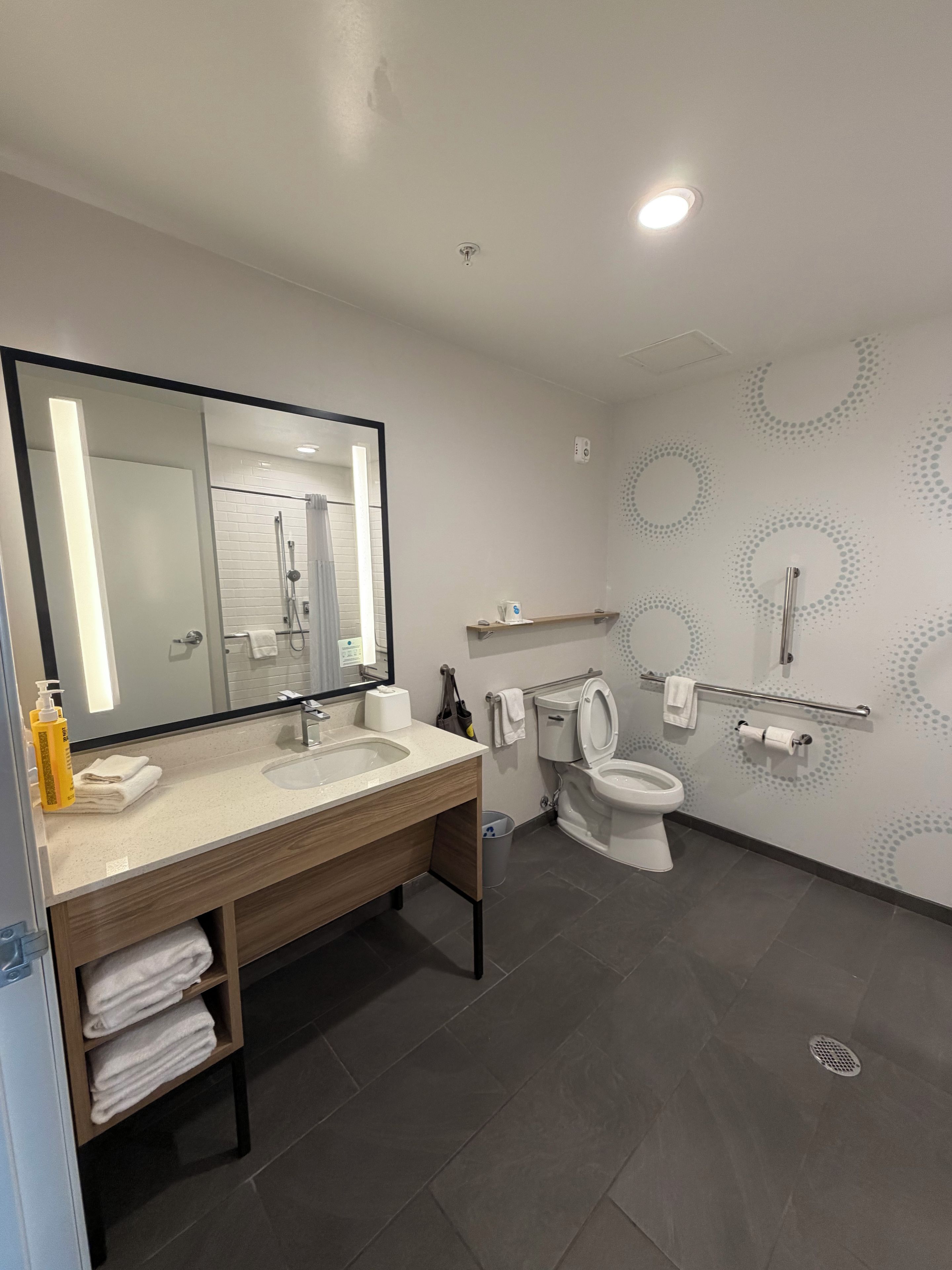 A modern bathroom with a large mirror, a sink, a toilet, and a shower area.