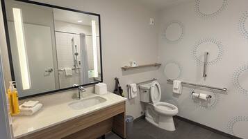 Un baño moderno con un espejo grande, un lavamanos, un inodoro y una zona de ducha.