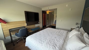 Una habitación de hotel con una cama, un escritorio con una silla, un televisor y un espejo.