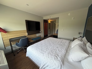 Une chambre d’hôtel comprenant un lit, un bureau avec une chaise, une télévision et un miroir.