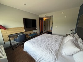 A hotel room with a bed, a desk with a chair, a television, and a mirror.
