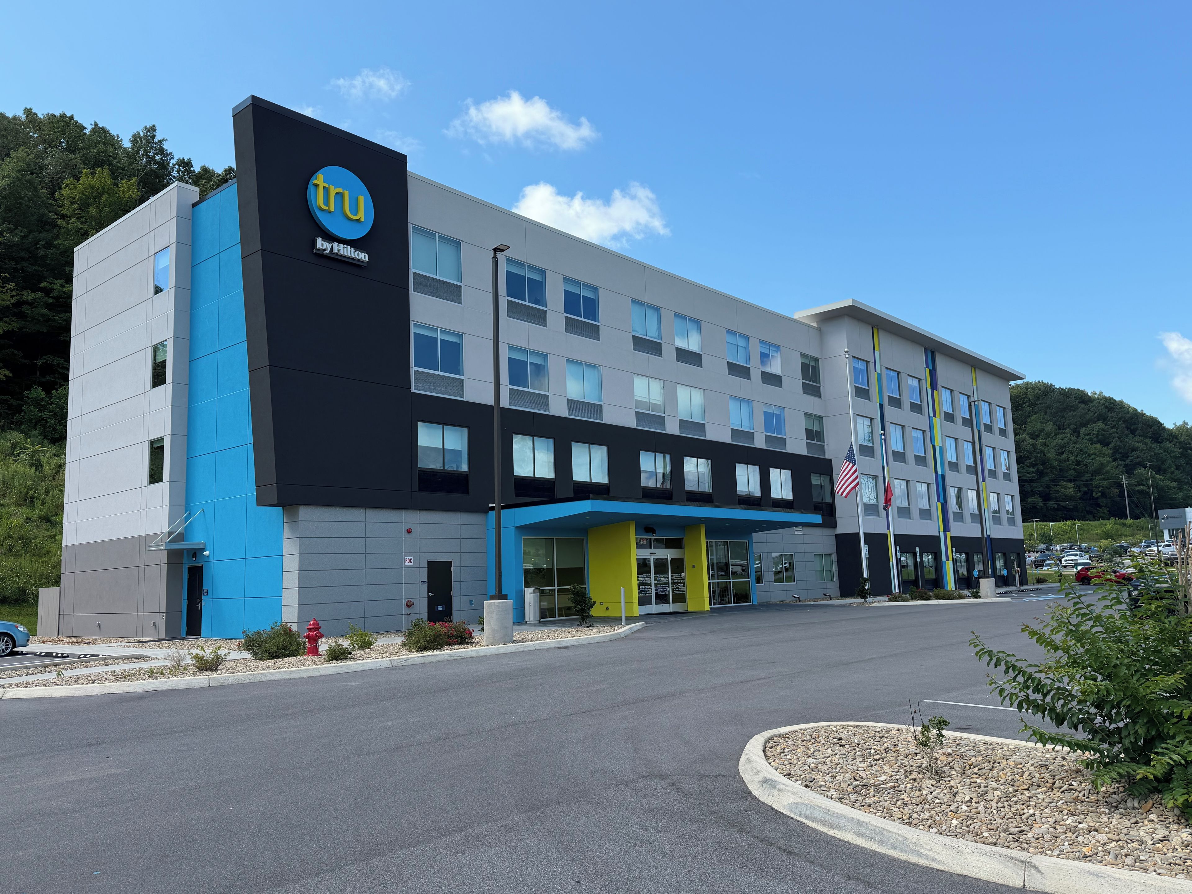 A modern hotel building with a prominent logo, multiple floors, and a parking area.