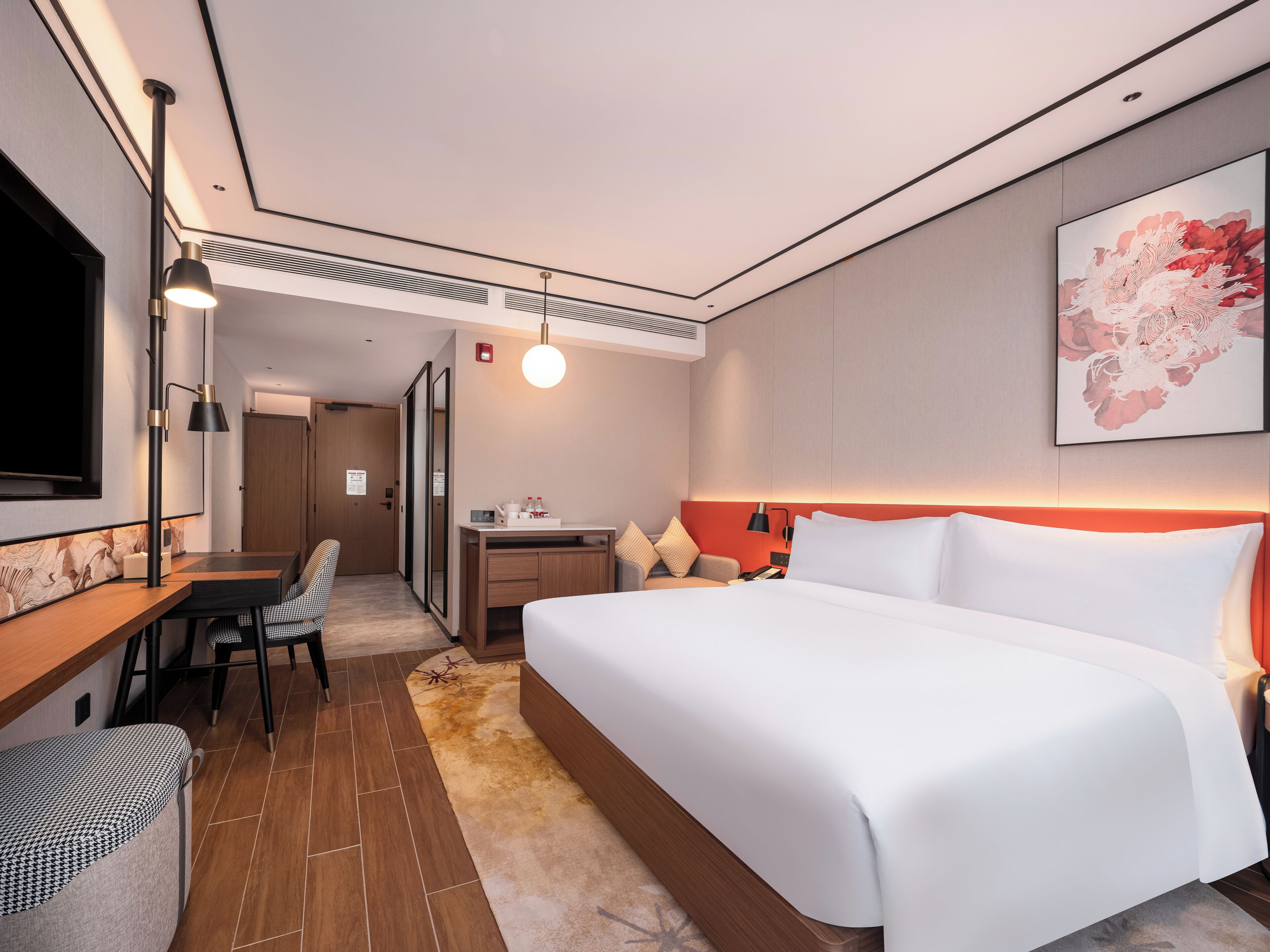 A modern hotel room with a large bed, a desk, a chair, and a television.