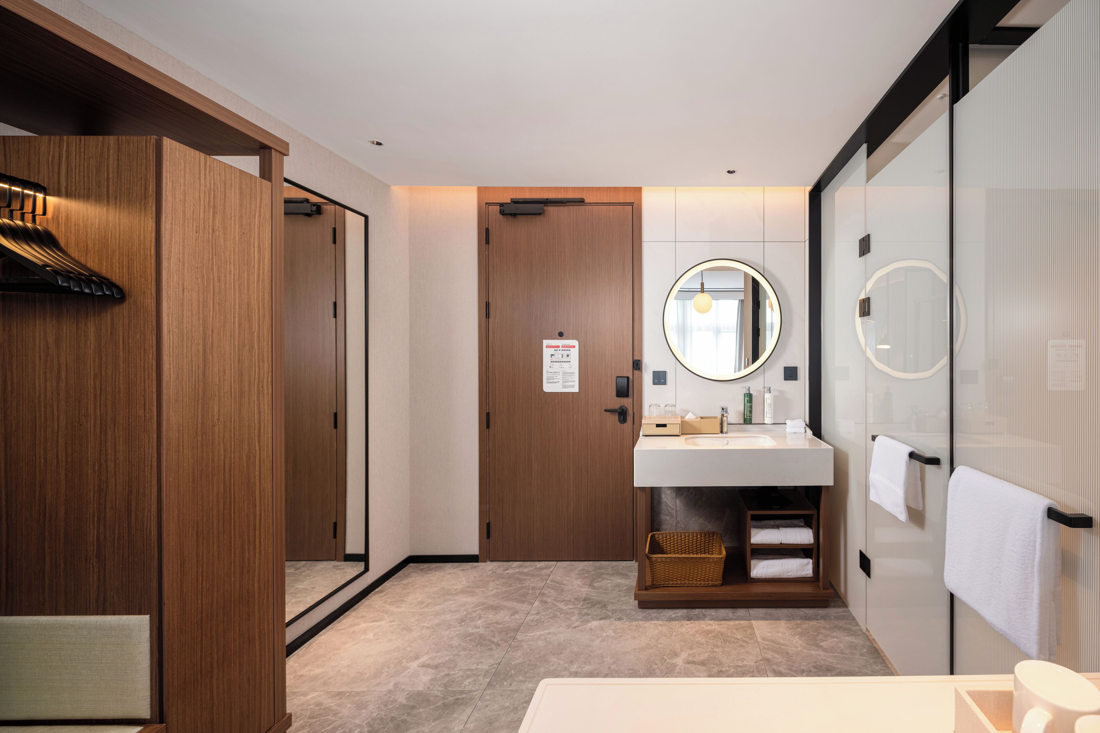 Ein modernes Badezimmer mit einem Holzbadezimmer-Möbel, einem runden Spiegel und einer Duschkabine aus Glas.