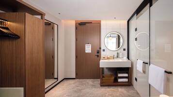 A modern bathroom with a wooden vanity, a round mirror, and a glass shower enclosure.