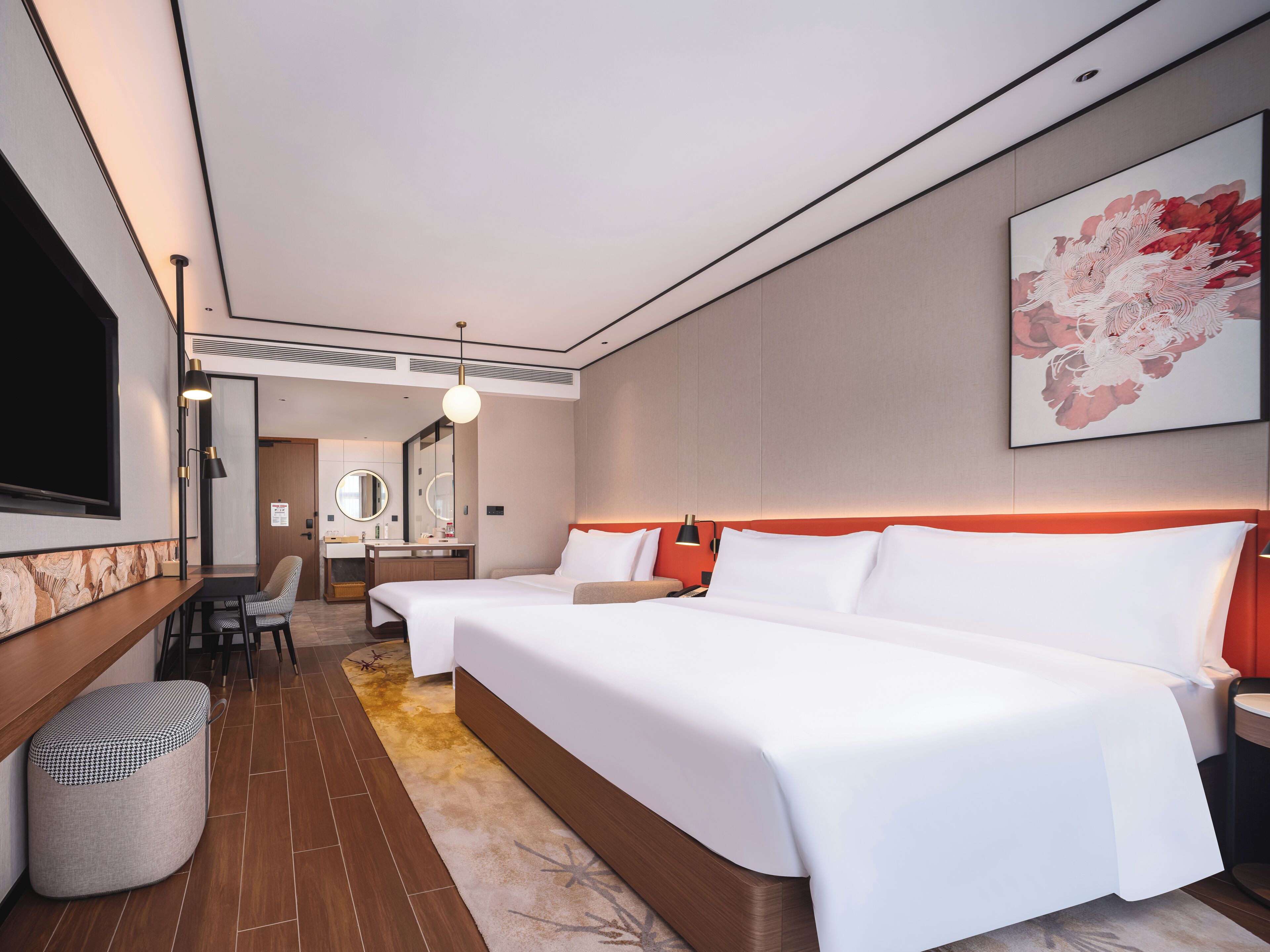 A hotel room with a large bed, bedside tables, a mirror, a desk with a chair, and a large artwork on the wall.