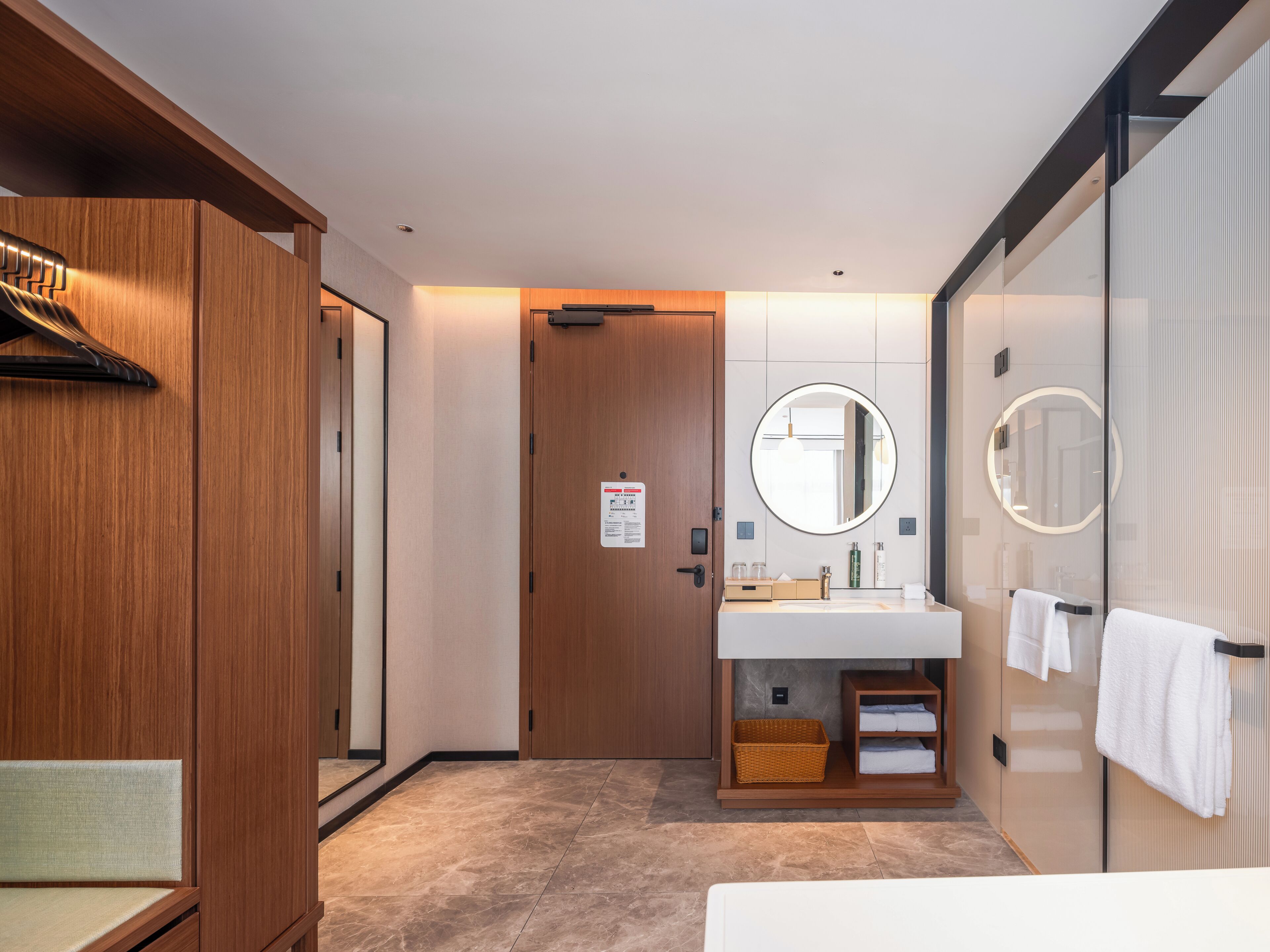 Een moderne badkamer met een houten wastafelmeubel, een ronde spiegel en een handdoekrek.