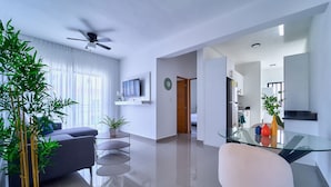 A modern living room with a sofa, a glass dining table, and a ceiling fan. - Cozy Nest (La Romana)