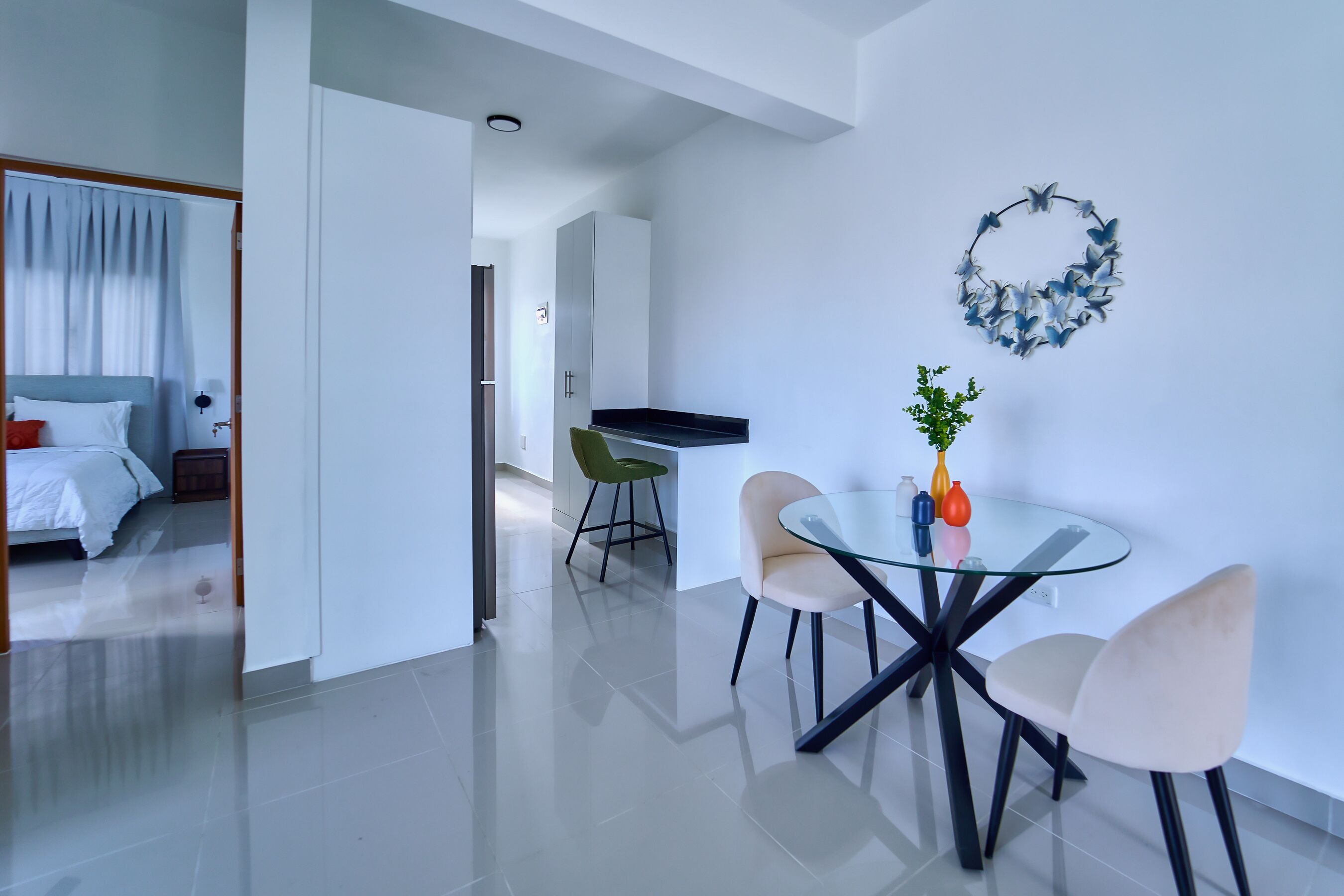 Een moderne hotelkamer met een bed, een zithoek met een glazen tafel en stoelen, en een kitchenette.