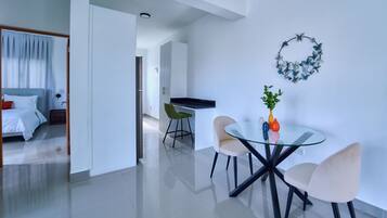 Een moderne hotelkamer met een bed, een zithoek met een glazen tafel en stoelen, en een kitchenette.