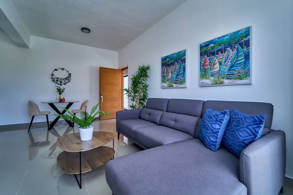 A modern living room with a grey sofa, blue patterned pillows, a wooden coffee table, and two paintings on the wall.