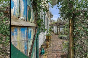 A narrow brick pathway flanked by overgrown vegetation and a weathered blue door.