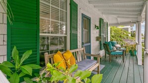Eine Veranda mit einer Holzbank und Stühlen, grünen Fensterläden und Topfpflanzen.