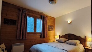 Un dormitorio acogedor con pared de madera, una cama doble, dos lámparas de noche y una ventana con cortinas.