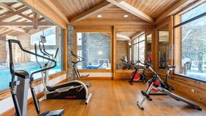 Un gimnasio con diverso equipo de ejercicio, amplias ventanas y decoración de madera.