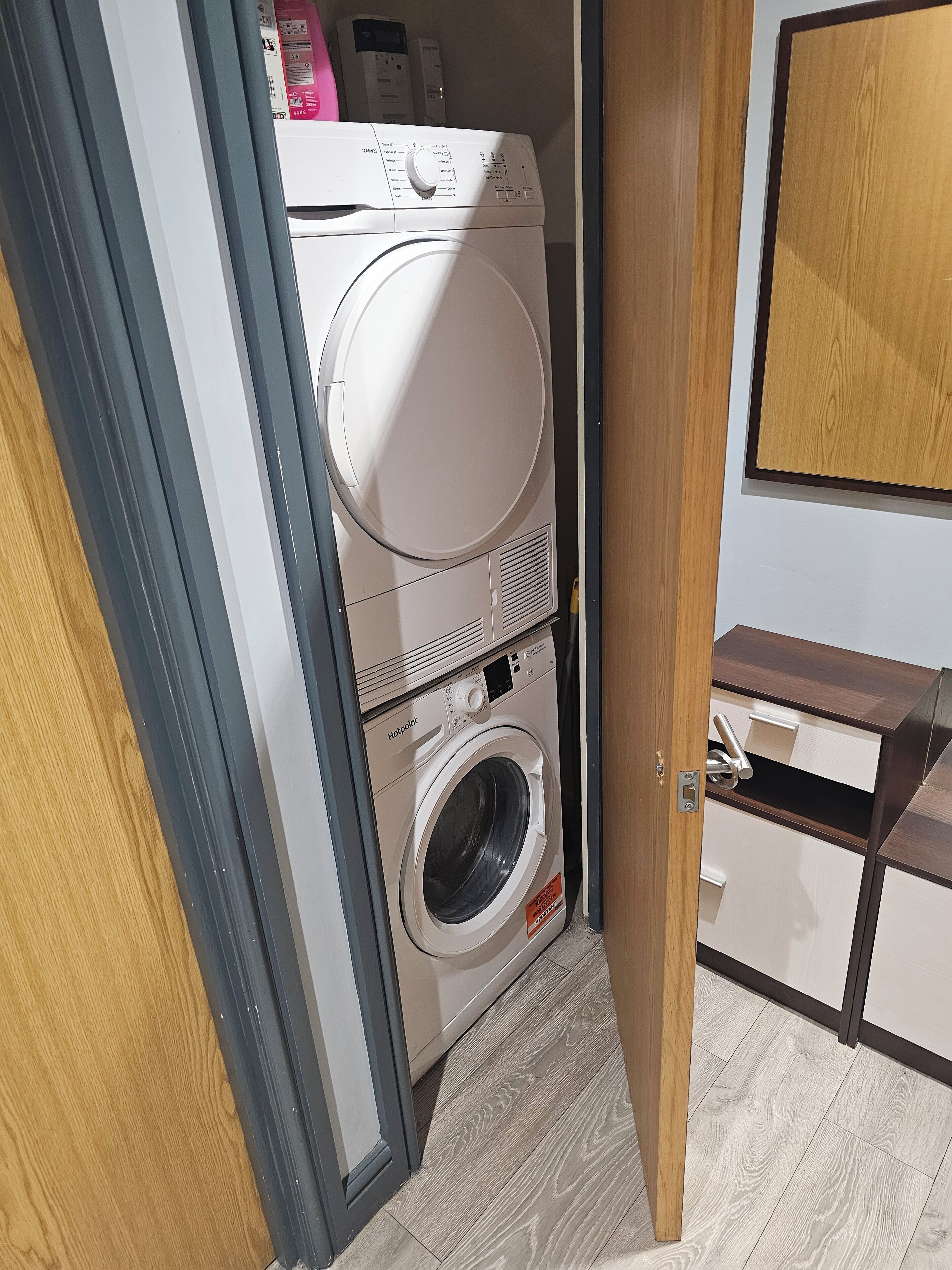 A laundry room with stacked washing machines and dryers, wooden cabinets, and a tiled floor.
