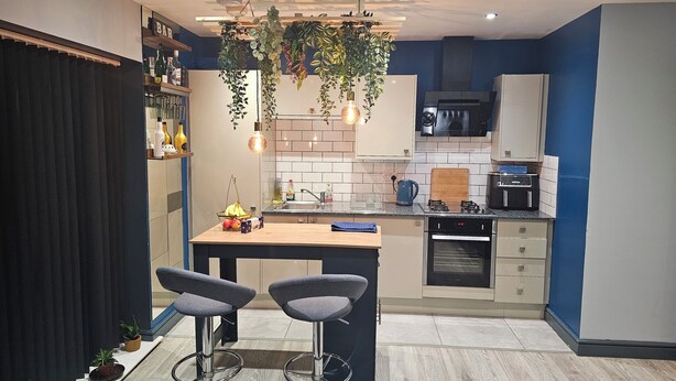 A modern kitchen with a central island, bar stools, hanging plants, and a variety of appliances. - Adorable 2-bedroom apartment in Southampton (Southampton)