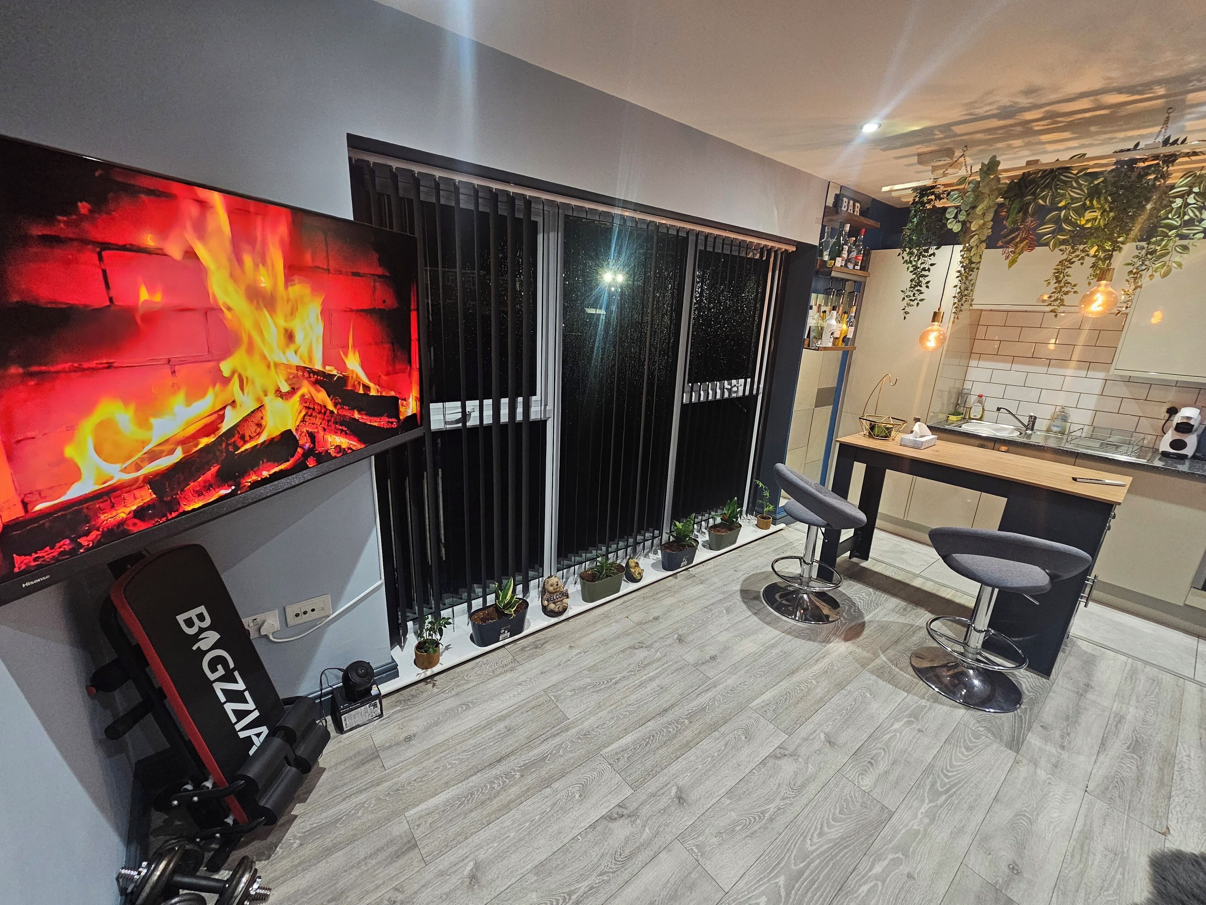 A modern kitchen with a bar area, a large TV displaying a fire, and a seating area with a bar stool and a chair.