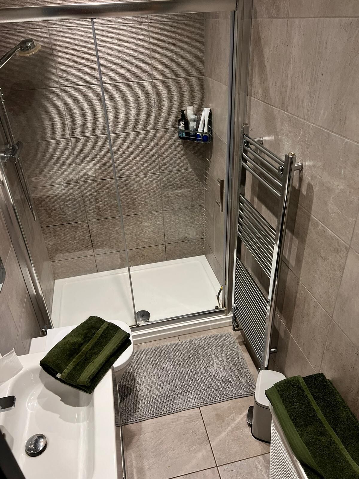 Un baño moderno con ducha de vidrio, una bañera blanca y una toalla verde sobre el lavamanos.
