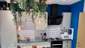 A modern kitchen with a wooden island, two bar stools, hanging plants, and a built-in oven. - Adorable 2-bedroom apartment in Southampton (Southampton)