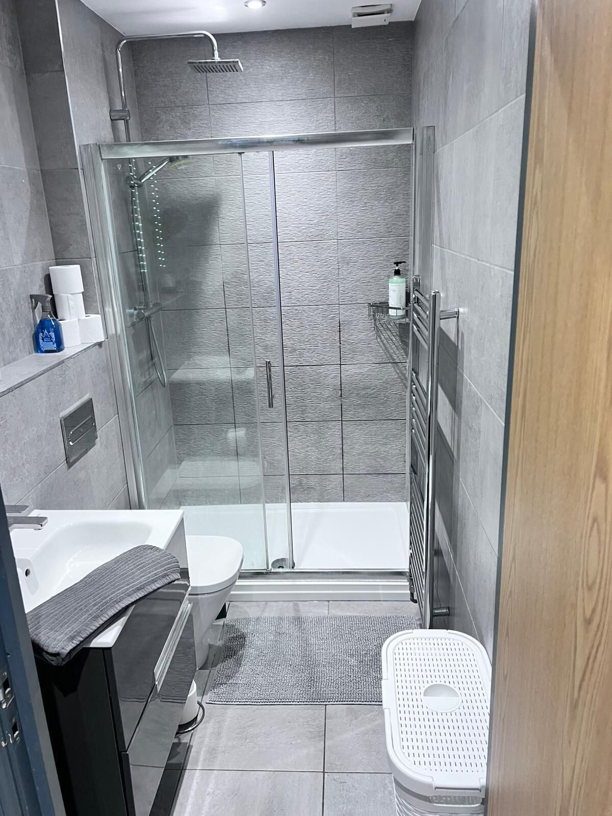 A modern bathroom with a glass-enclosed shower, a white toilet, a sink with a towel, and a small trash bin.