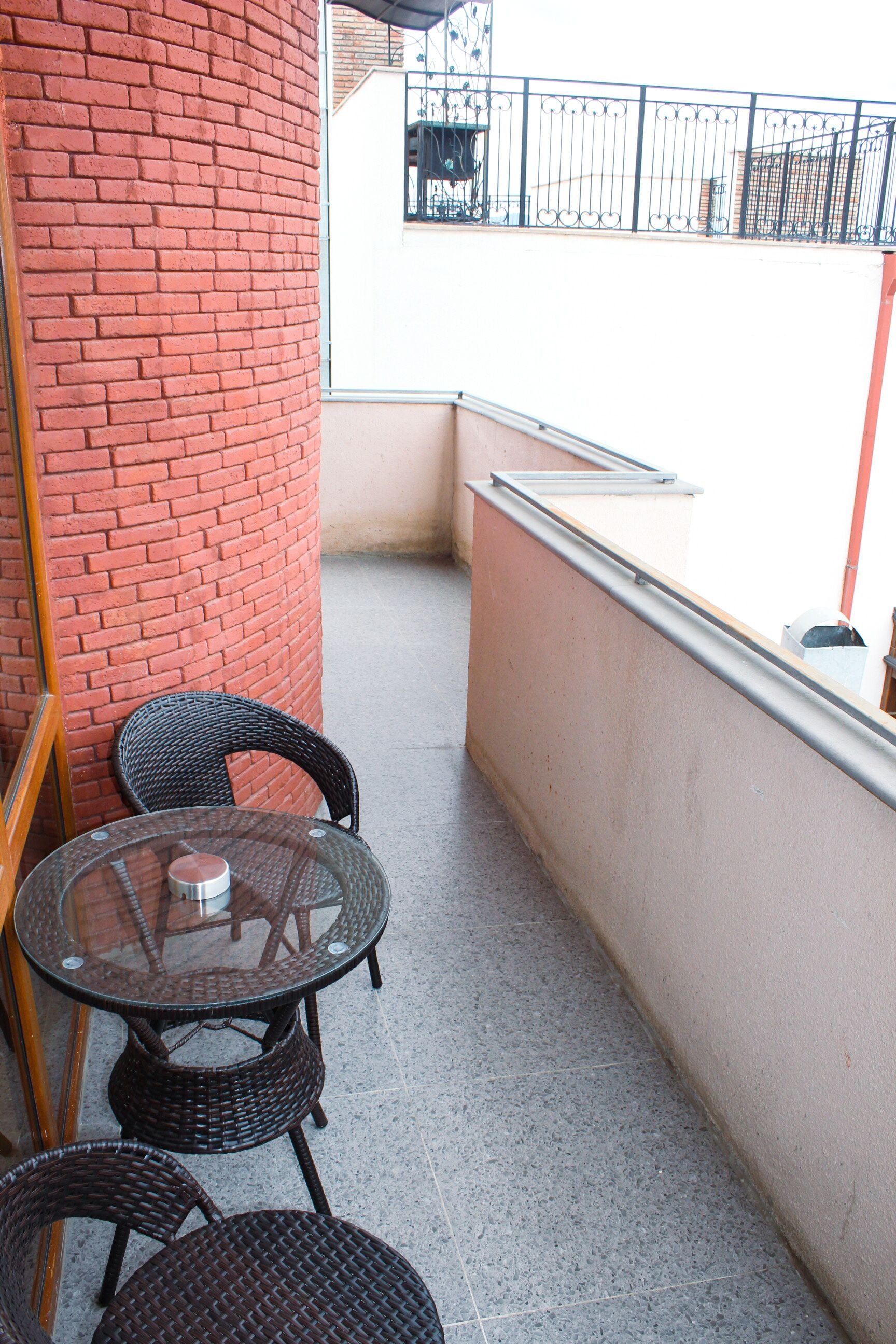 A small outdoor seating area with wicker chairs and a glass table, adjacent to a red brick wall.