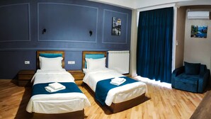 A hotel room with two beds, wooden flooring, a blue accent wall, and a blue chair. - Hugo Boutique Hotel (Tbilisi)