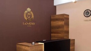 A reception desk with a logo, a clock, and a modern light fixture. - Hugo Boutique Hotel (Tbilisi)