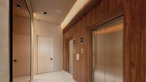 A modern hallway with a wooden wall panel, a white door, and a metallic elevator. - Modern Loft in 85st near Andino (Bogotá)