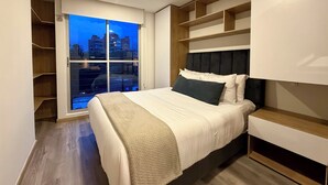 A modern bedroom with a large bed, built-in shelving, a view of the cityscape through a window, and a wooden floor. - Modern Loft in 85st near Andino (Bogotá)