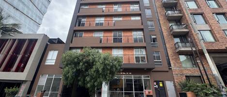 A multi-story building with a modern architectural design, featuring a mix of brick and glass facades, and a central entrance with a bench.