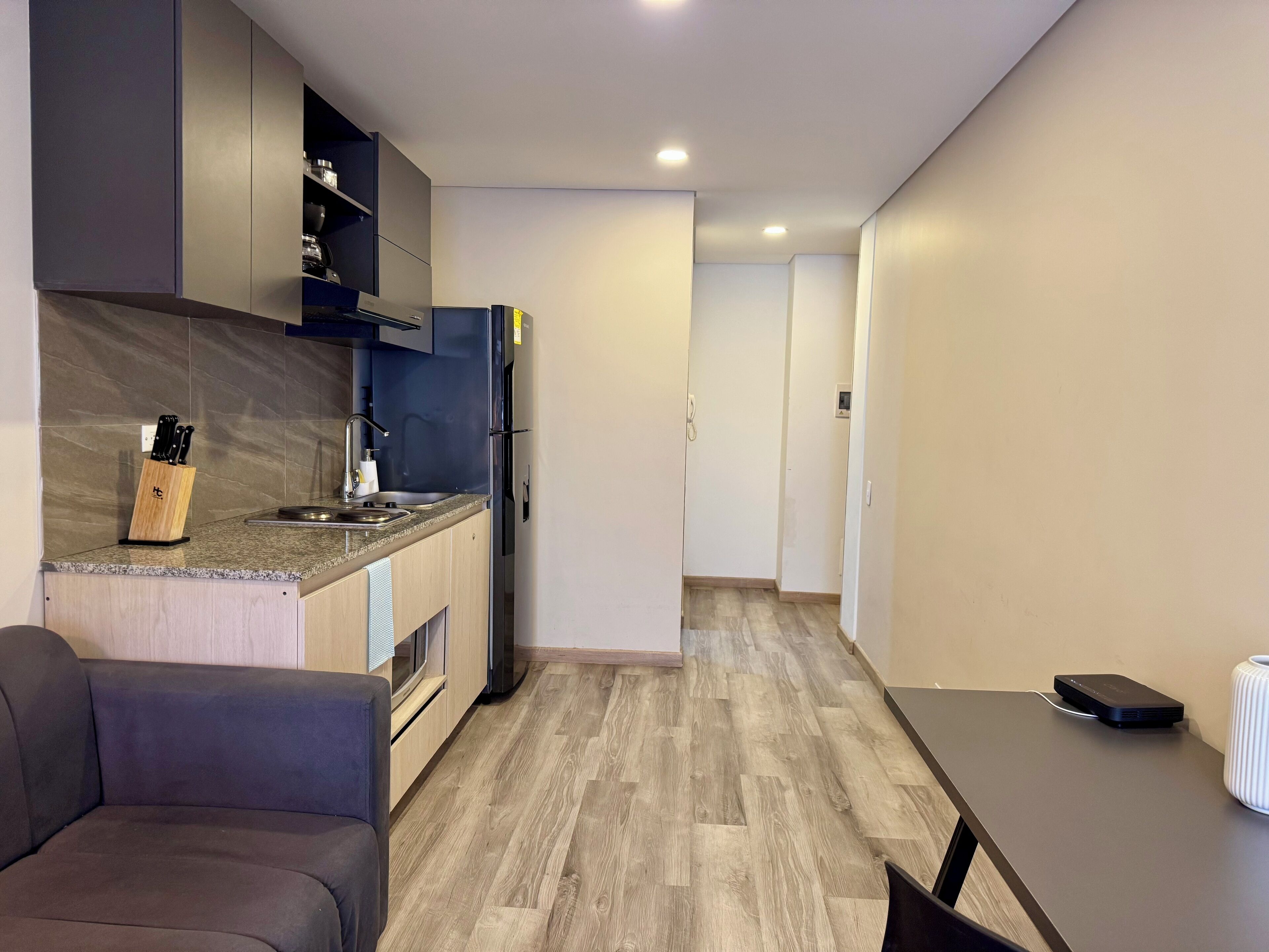 A modern kitchen with a built-in oven, a sink, and a refrigerator. There is a wooden dining table with chairs and a small white vase.