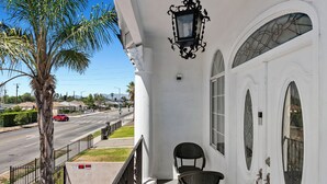 A white building with a balcony, a palm tree, and a street view.