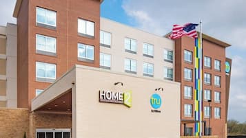A hotel with a modern design, featuring a prominent American flag, a sign for 'HOME 2 Suites by Hilton,' and a logo for Tru by Hilton.