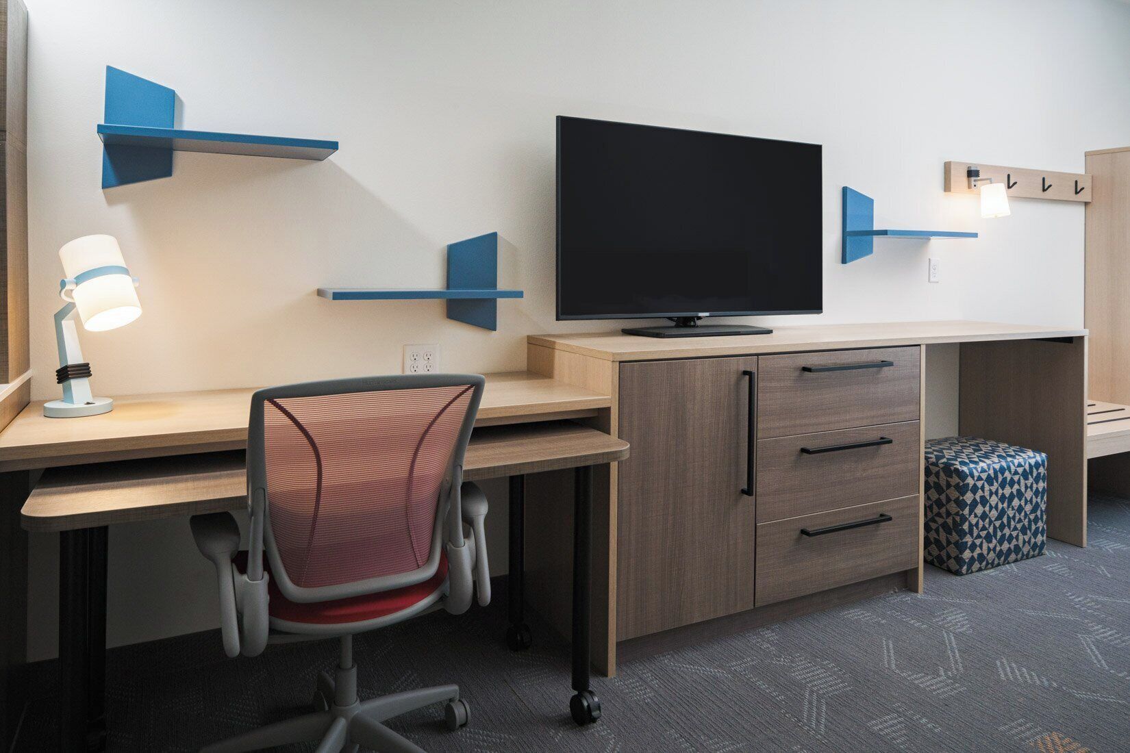 A modern office desk with a flat-screen TV, a desk lamp, and a chair.