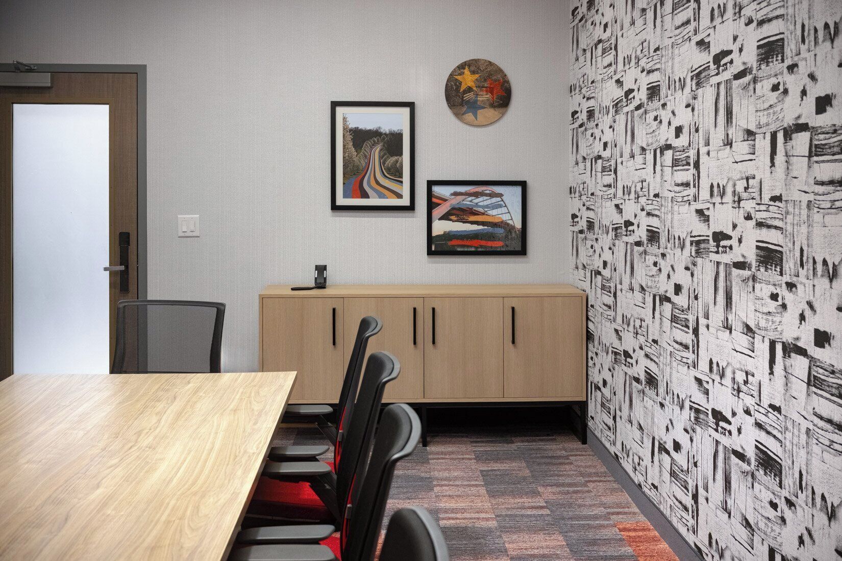 A conference room with a wooden table, black chairs, a light-colored cabinet, and two framed artworks on the wall.