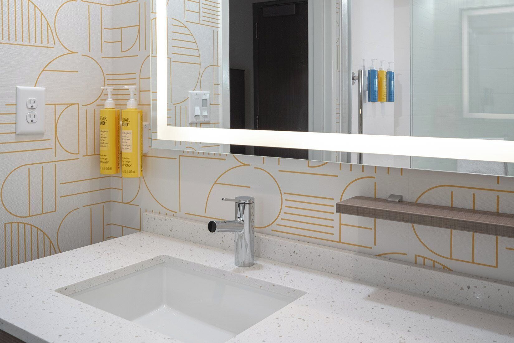 A bathroom with a white sink, a mirror, and a patterned wall.