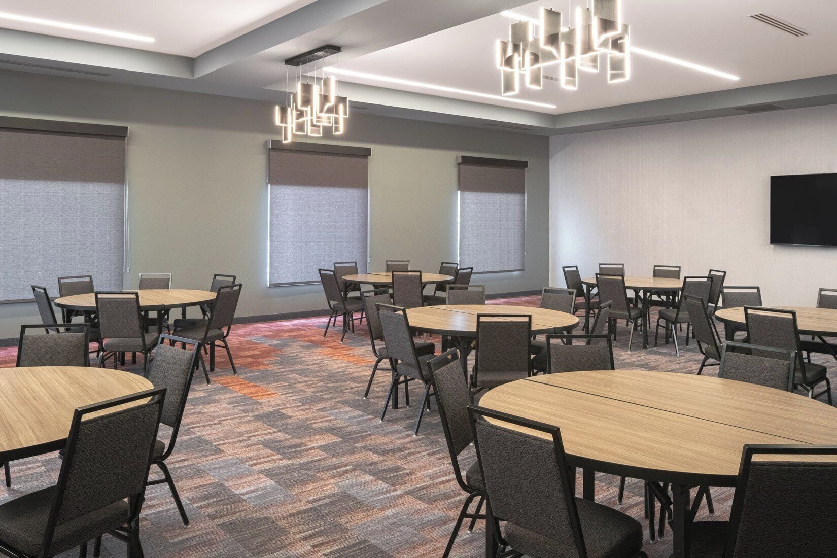A conference room with round tables, chairs, a projector screen, and a flat-screen TV.