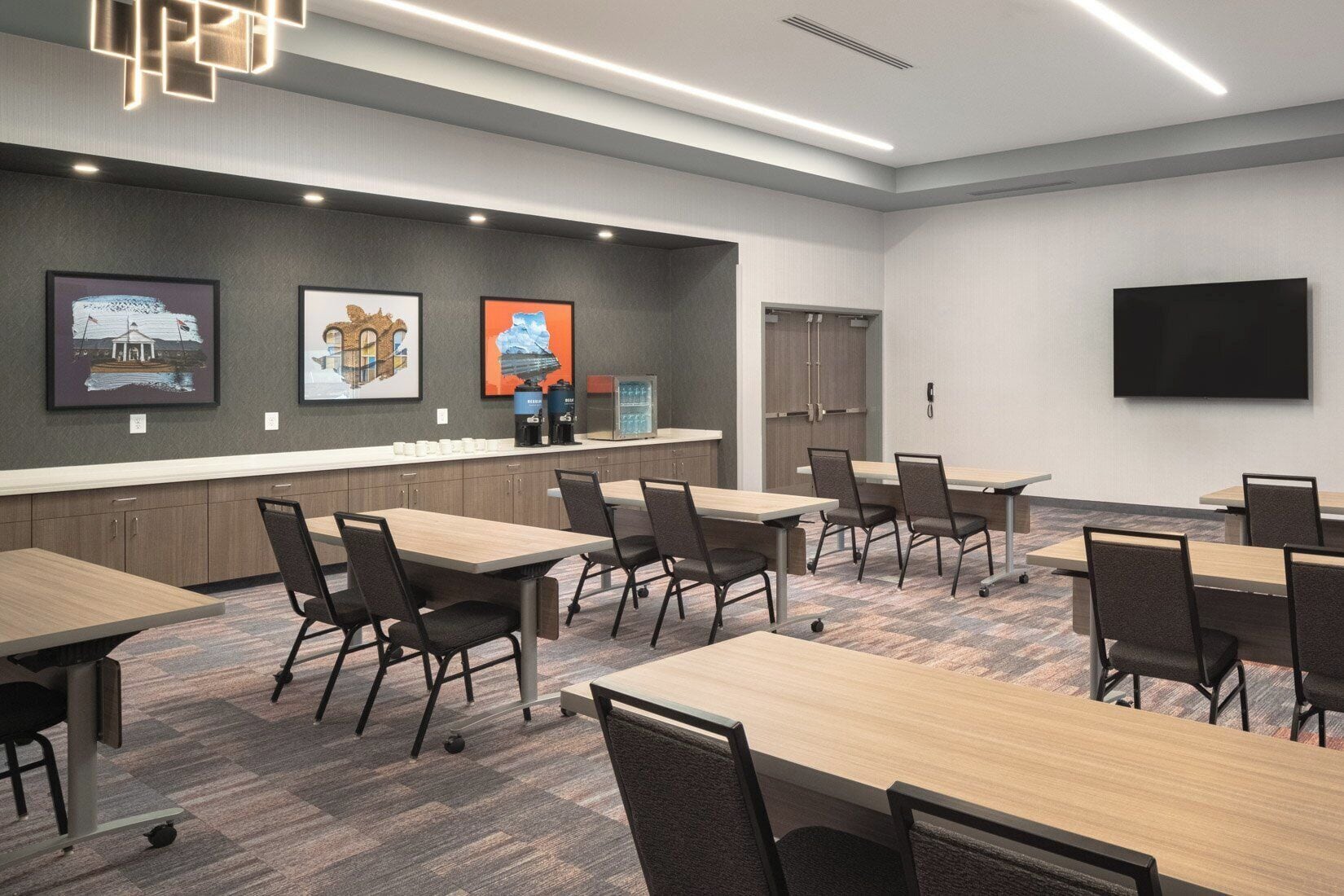 A conference room with tables, chairs, a flat-screen TV, and artwork on the wall.