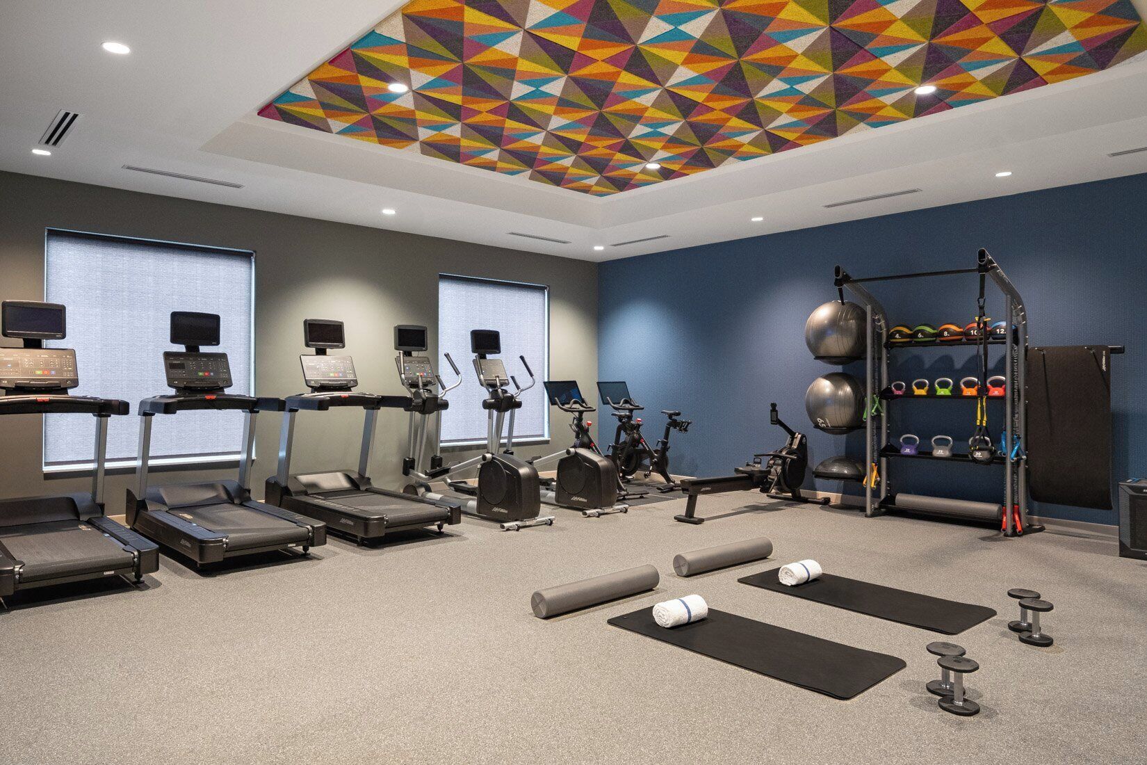 A gym with treadmills, elliptical machines, stationary bikes, and a weight rack.